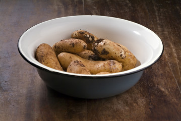 dirty potatoes in an old bowl on a wooden table