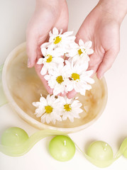 female hands in bowl full of water and flower
