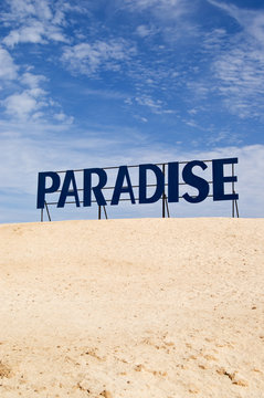 Paradise guide board between desert sand and blue sky