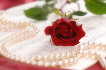 Red rose and string of pearls lying on sheet music