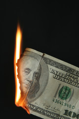 One hundred dollars bill on fire over black background