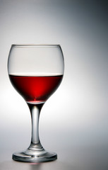 Footed glass of red wine over grey background