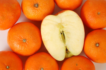 A sliced apple among orange tangerines on white.