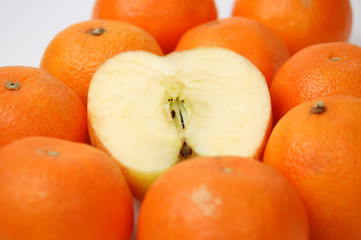 A sliced apple among orange tangerines on white.