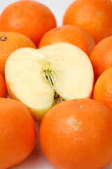 A sliced apple among orange tangerines on white.