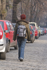 Redheaded girl with a backpack walking past a row of cars.