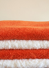 Stack of white and orange fluffy towels on light background