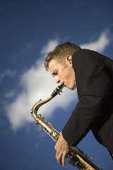 Young saxophone player playing his instrument outdoors.