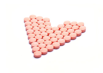 Pink pills ordered in a shape of heart on white background