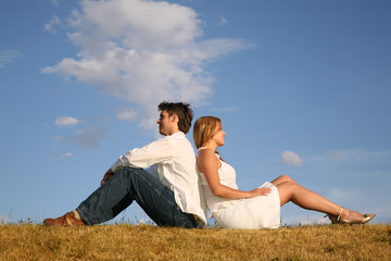 couple sit on meadow back to back