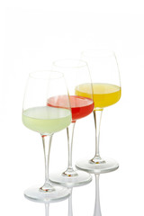 Three glasses with beverages, reflected on white background