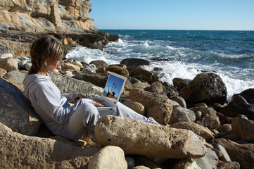 girl on the rocks near the sea relaxing and using a laptop