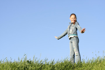 Girl costs on a grass on a background of the blue sky