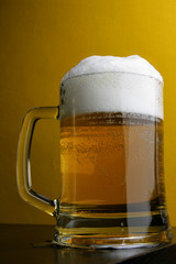 Beer mug with froth over yellow background