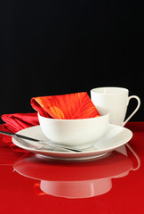 A modern table setting with white dishes and a red background
