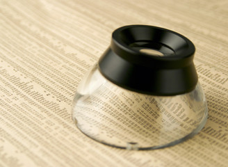 Magnifying loop resting on financial newspaper