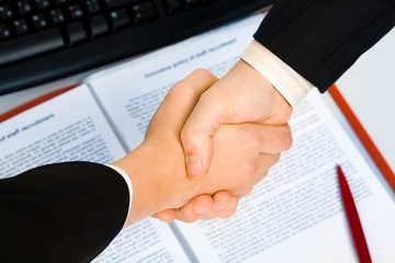 View of handshake over contract with pen in the background