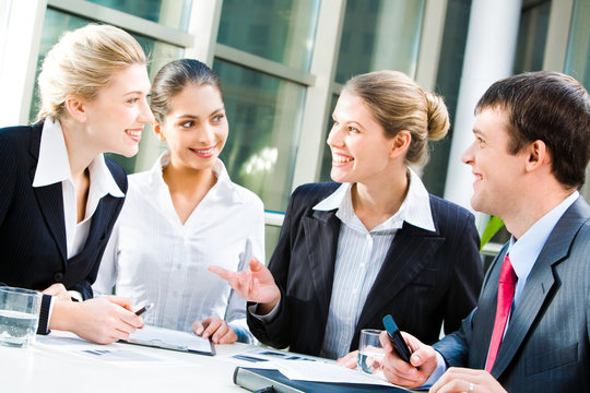 Medium shot of young Caucasian male and female managers sitting at table and discussing business project at work in office