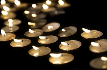 Burning tea lights on black background, with selective focus