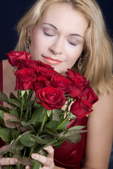 Beautiful blond woman hugging red roses and smelling them