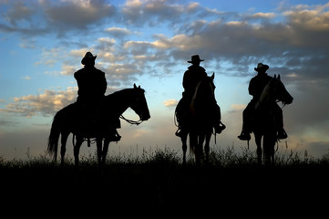 Three cowboys on horseback silhouetted against dawn sky