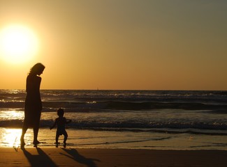 young woman with small child on the sea shore on sunset