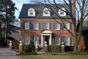 two storey brick house with dormers, shutters, and hedge