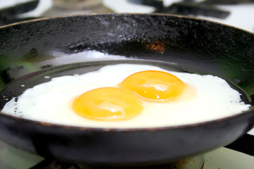 Two fried eggs in hot pan on gas stove
