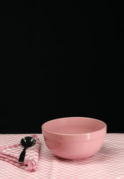 A pink picnic table setting with bowl, spoon and napkin