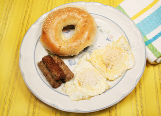 Eggs over easy, sausage and buttered bagel on yellow mat