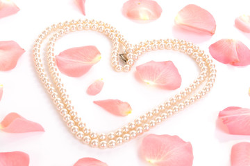 Heart shaped from string of pearls among pink rose petals