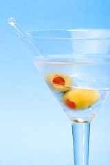 martini in glass with two olives over aqua background.