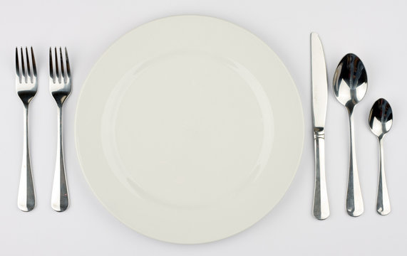 A Place Setting For A Dinner Against A White Tablecloth