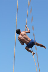Shirtless athlete climbing up the rope