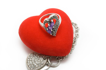The silver ring with violet stones lays on red velvet heart.