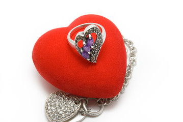 The silver ring with violet stones lays on red velvet heart.