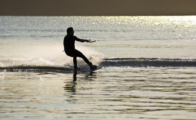 sunset waterskiing wakeboarder sprays water into the air. 