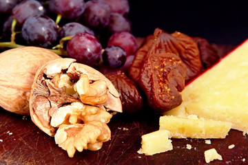 A board with walnuts, red grapes, figs, and sharp cheese.