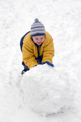 Fototapeta na wymiar The boy rolls snow whom in winter day