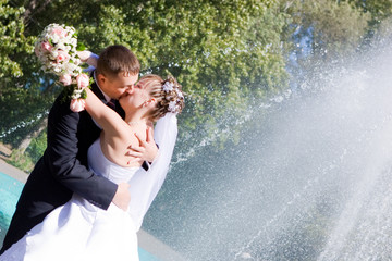 a bride and a groom kissing near the fountain