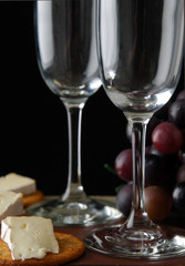 Two empty wine flutes by grapes and brie cheese