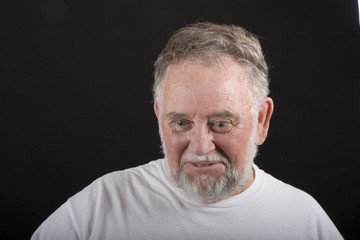 An older man in white tshirt on a black background looking down