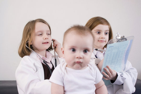 Six and seven year old girls playing doctor with a baby.