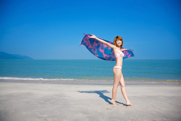 Naklejka na ściany i meble young woman in bikini holding floral scarf walking by beach