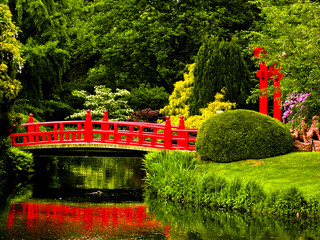 Red bridge over a lake in green japanese garden