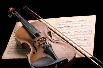old violin with fiddlestick on music sheet isolated on black