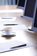Image of cup, papers, pens and monitors placed on a table