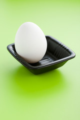 White egg on the small black cup over a green background