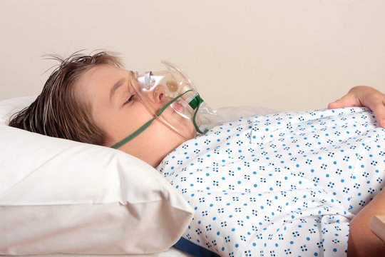 Child resting in bed has an oxygen mask or inhaler over face.