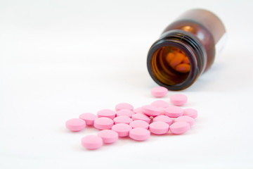 Pink pills scattered and bottle of brown glass isolated on white